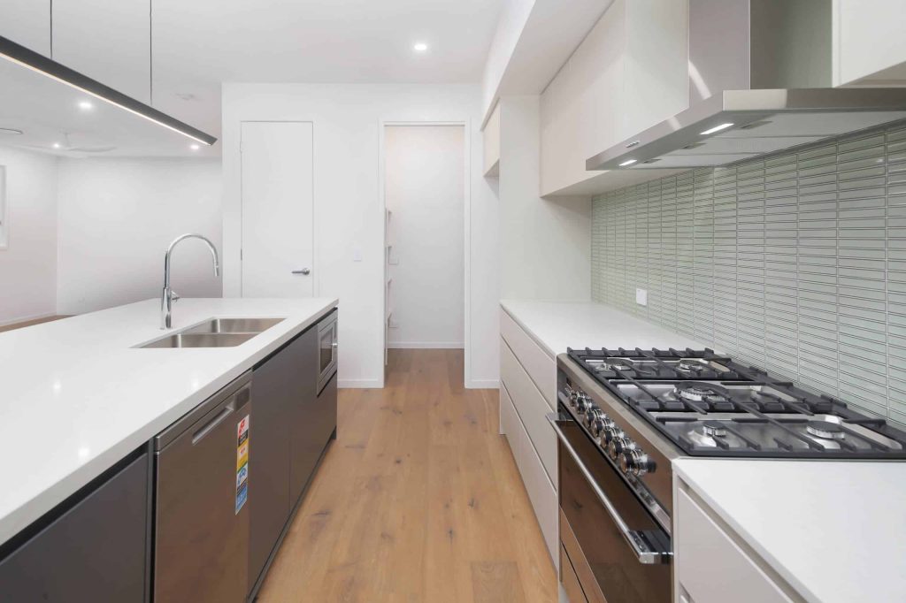 Galley kitchen with gas cooktop, island sink and dishwasher in an Alderley custom home