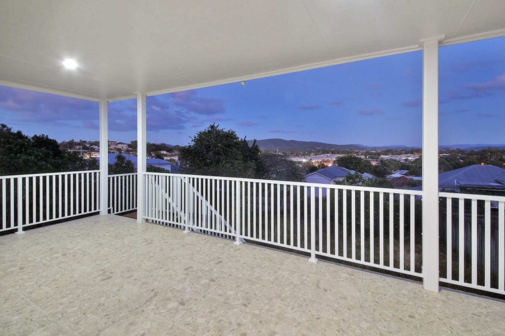 Covered balcony with white balustrade and suburban hillside views in an Alderley custom home