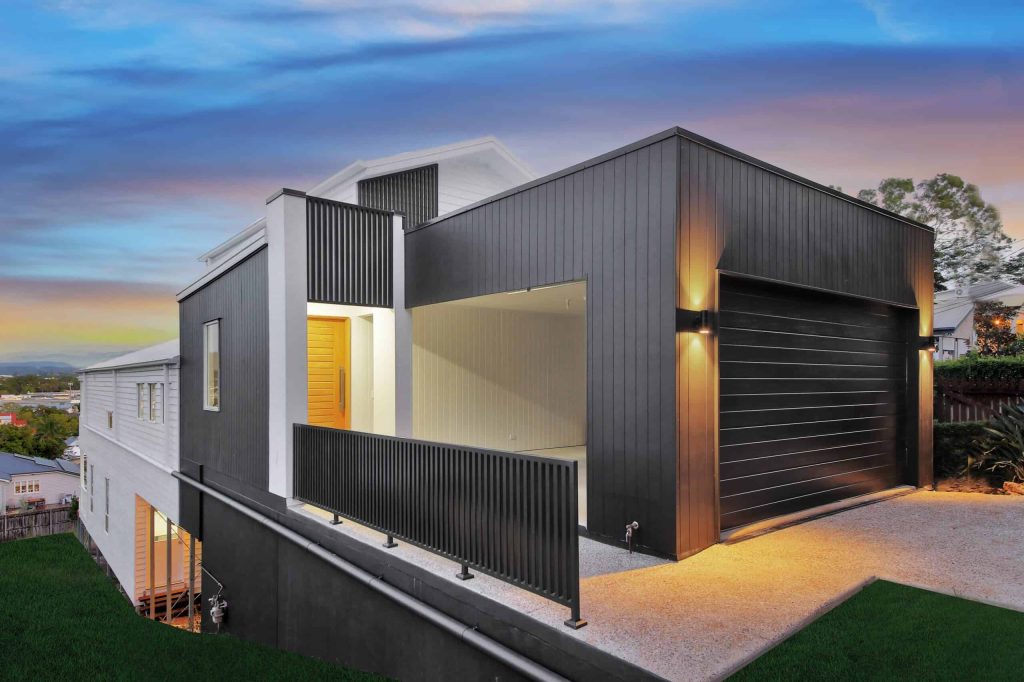 Contemporary two-storey home with dark cladding on a sloping block in Alderley at dusk