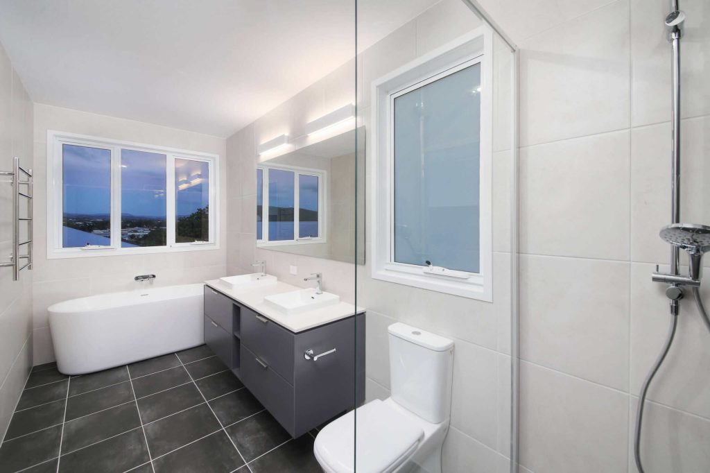 Main bathroom with freestanding bath, glass shower and grey vanity in an Alderley custom home