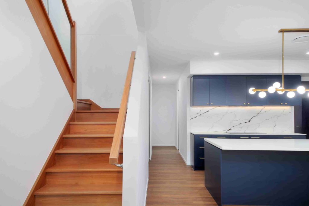Timber staircase leading to kitchen with navy cabinetry in a Sunnybank custom home
