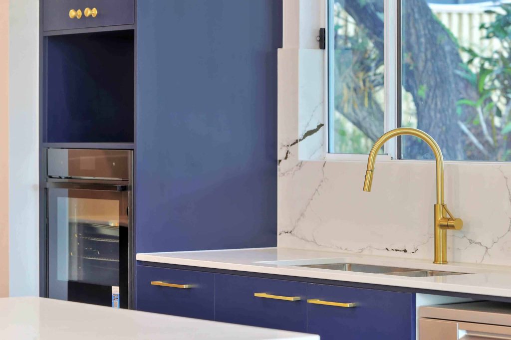 Gold gooseneck tap and navy cabinetry with wall oven in a Sunnybank custom home kitchen